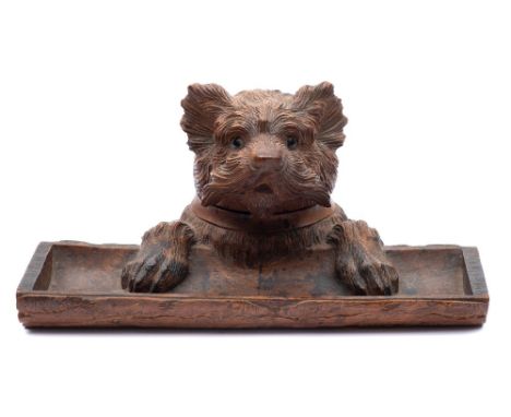 A Black Forest carved linden wood inkwell: in the form of a terrier dog holding onto a log , the hinged head with inset glass