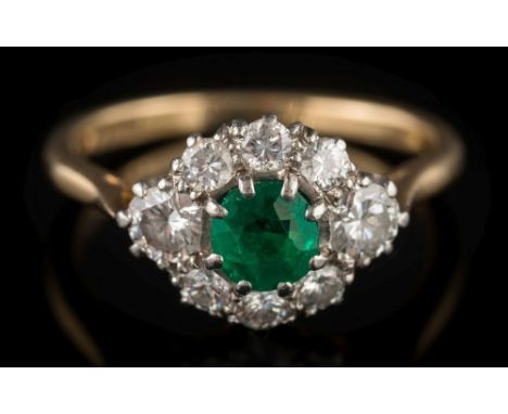 An emerald and diamond cluster ring: the central round emerald approximately 4.5mm diameter x 3.2mm deep, within a surround o
