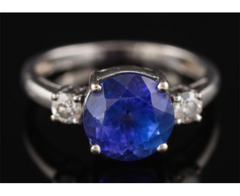 A modern tanzanite and diamond ring: the round tanzanite approximately 8.7mm diameter x 6.2 mm deep, in four claw setting and