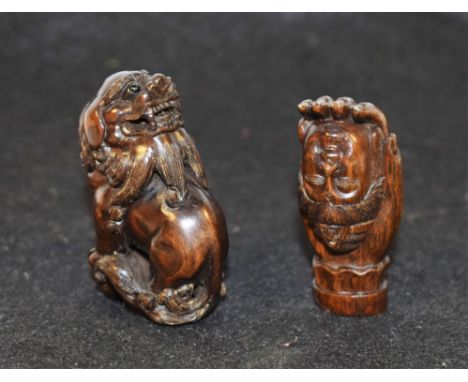 A Japanese hardwood netsuke, carved as a komainu, both its front paws resting on a sphere, 5cm long; another, a deity's head 