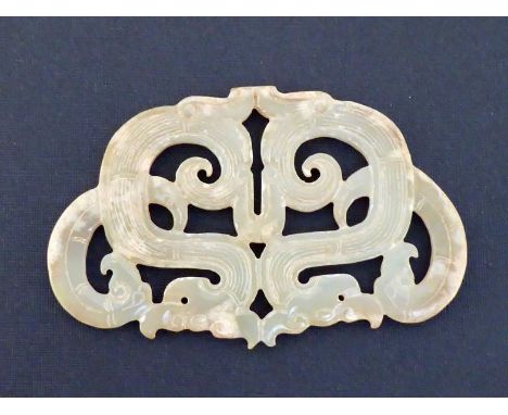 A Chinese archaic style carved jade pendant of escutcheon form, modelled as four scrolling dragons, with occasional cream-col