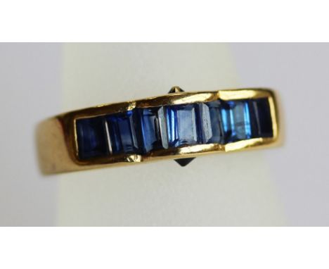 AN 18K GOLD AND SAPPHIRE SET RING, the shaped face set with seven baguette cut stones (ring size K - gross weight 6 grams) CO