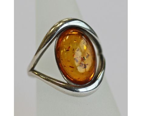 A 925 GRADE WHITE METAL AND AMBER RING, an oval amber cabochon set in a shaped open surround, marked 925, ring size K. 4grams