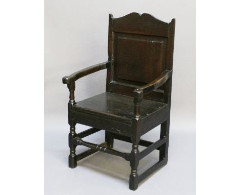 AN OAK WAINSCOT TYPE ARMCHAIR 18th century and later, with yoke-form crest-rail, fielded panel back and shaped open arms, the