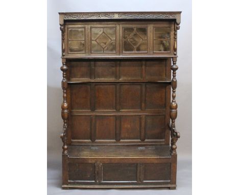 A LATE 19TH CENTURY PANELLED OAK HALL SETTLE having a canopy with S-scroll carving, turned pendants, glazed cupboard doors, p