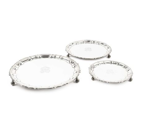 A set of three Edwardian graduated silver salvers, with shaped piecrust borders, on foliate scroll feet, by William Hutton &a