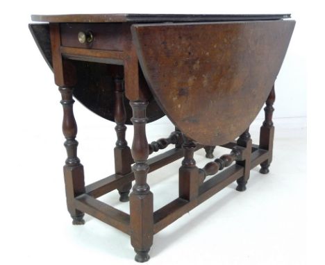 An 18th century oak drop leaf table, oval surface, single drawer with brass knob, turned supports with kick leg action and pe