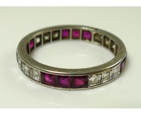 A white gold, ruby and diamond eternity ring, the scroll engraved band set with twelve emerald cut diamonds and twelve square