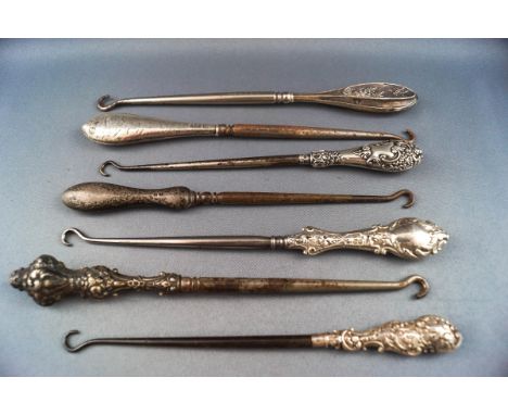 Seven button hooks each with silver handles, four embossed with C scrolls and foliage, another with a butterfly hovering over