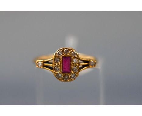 A yellow gold dress ring set with a central rectangular ruby and twelve round brilliant diamonds. Yellow split design shoulde