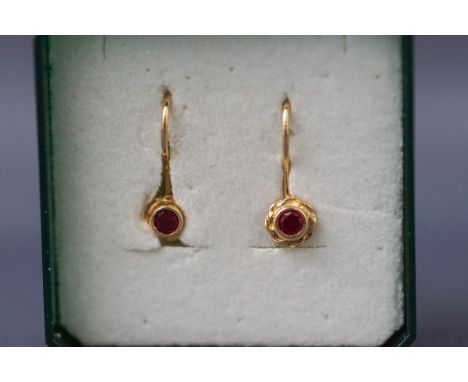 A yellow gold pair of single stone earrings having continental hook fittings. Each set with a round synthetic ruby. Tests ind