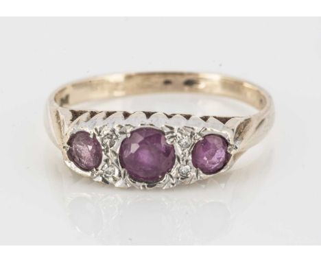 A 9ct gold ruby and diamond dress ring, three round cut rubies flanked by pairs of eight cuts within a white metal ovoid sett