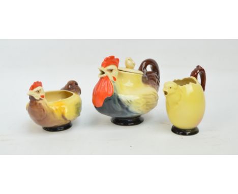 A Royal Doulton three piece tea service comprising a cockerel teapot with chick lid, a hen sugar bowl and a chicken and egg m