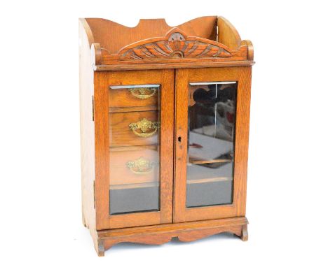 An Edwardian oak smoker's cabinet with two glazed doors enclosing three drawers and a shelf, width 33cm.