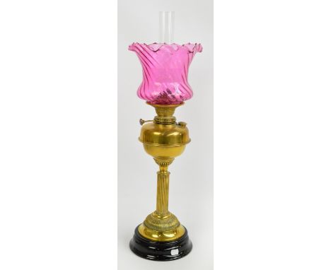 A late Victorian brass oil lamp with cranberry tinted wrythen moulded glass shade above plain reservoir and fluted central co