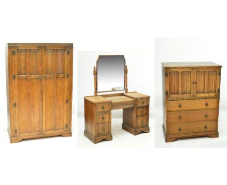 A mid 20th century oak linen fold decorated three piece bedroom suite comprising wardrobe, tallboy and dressing table (3).