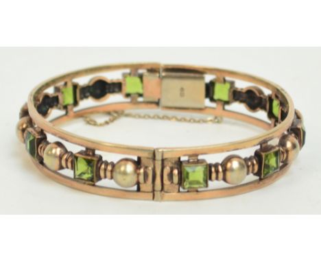 A peridot set pierced yellow metal snap bangle, the ten square cut stones set amongst circular decoration, diameter 6.5cm.