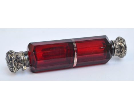 A Victorian ruby faceted glass double ended scent bottle with white metal mounts embossed throughout with foliated scrolls, l