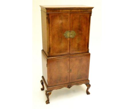 A mid 20th century walnut cocktail cabinet, the moulded cornice above pair of cupboard doors with brass mounts, above further