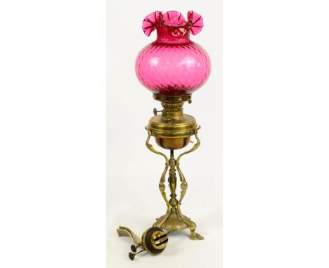 An Art Nouveau brass oil lamp, with cranberry tinted glass shade on stylised floral supports and base, converted to electrici