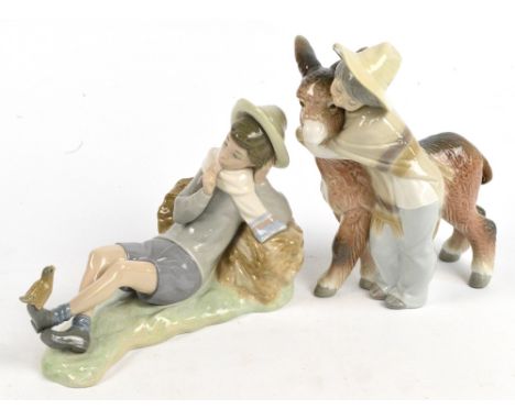 Two Lladro figures, one depicting a boy hugging a donkey, height 19.5cm, the other depicting a boy reclining on a haystack wi