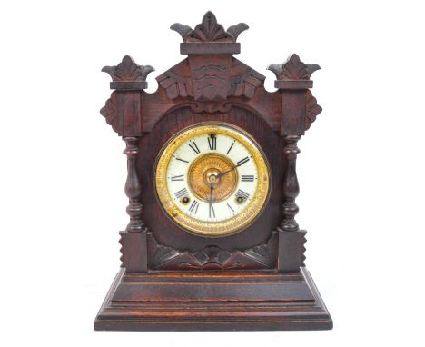 An early 20th century oak cased American mantel clock with turned spindle sides and carved panels and finials on stepped plin