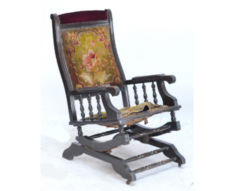 A late Victorian American style elbow rocking chair with turned spindle arms and stretchers, shaped reeded legs to castors, w