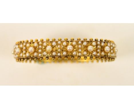 An Edwardian unmarked yellow metal snap bangle, one half floral set with seed pearls, with beaded edge, 6 x 5cm, approx 21g. 