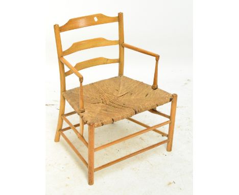 A low Arts and Crafts style ladder back rush seated elbow chair.