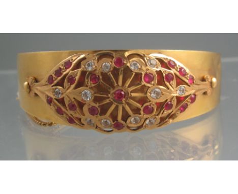 UNMARKED YELLOW GOLD SYNTHETIC RUBY BANGLE. The hinged bangle tapering in width from 20mm - 6mm, decorated with a pierced sty
