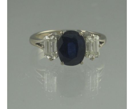 AN 18CT WHITE GOLD THREE STONE SAPPHIRE AND DIAMOND RING. The central oval sapphire approx 7 x 6mm set with a step cut diamon