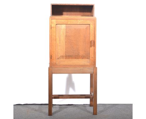 A small Arts &amp; Crafts oak cabinet on stand, Cotswold school, serving a bedside cupboard, open recess above a single cupbo