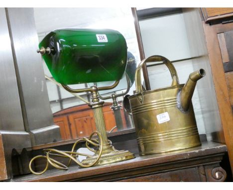 A brass bankers style table lamp with green shade and a brass watering can 