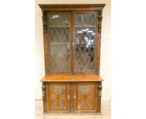 A Victorian carved oak leaded glazed two door book case standing on a cupboard base with carved doors 4' wide 