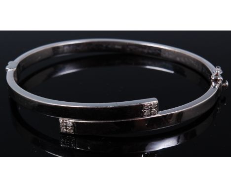 A modern 9ct white gold hinged bangle, the tips each set with four small brilliant cut diamonds, 10.7g, dia.6.5cm