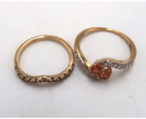 Two 9ct gold garnet rings. To include a two stone crossover ring with white zircon shoulders, size M 1/2. An eleven stone wis