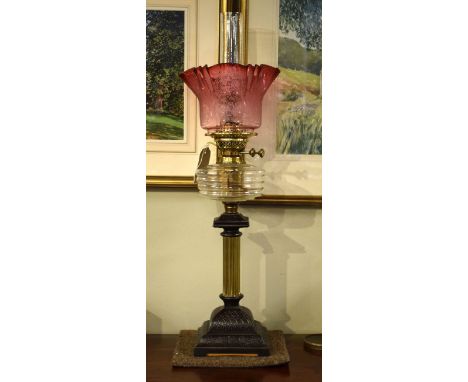 Victorian oil lamp having a clear glass reservoir, reeded brass and cast iron base with stylised foliate decoration, etched p