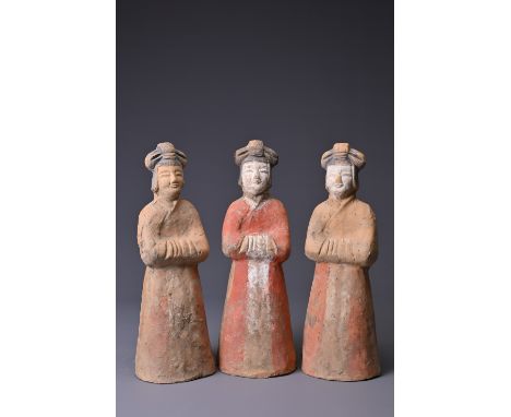 THREE CHINESE PAINTED POTTERY FIGURES OF ATTENDANTS, TANG DYNASTY (AD 618-907). Modelled standing wearing long flowing red st
