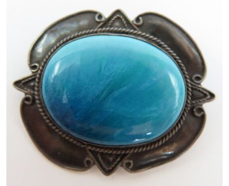 An Arts &amp; Crafts brooch, the ceramic oval centre in tones of turquoise and teal, with a twisted rope decoration around an