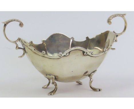 A silver sugar basin, by C C Pilling, London 1903, of oval panelled form, with flying leaf capped scroll handles and on four 