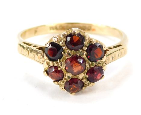 A 9ct gold garnet cluster ring, set with seven garnet stones in a patterned ring head, on hatch design shoulders with pierced