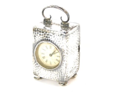 A miniature Edwardian hammered silver carriage type clock, the white dial bearing Roman numerals, the brass clockwork movemen