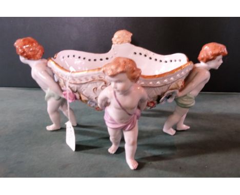 A German porcelain table centre, the oval central basket supported by four children, having flower encrusted decoration, hand