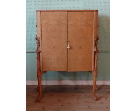 A mid 20th century walnut cocktail cabinet, the two cupboard doors revealing a two shelf mirrored interior, the sides having 