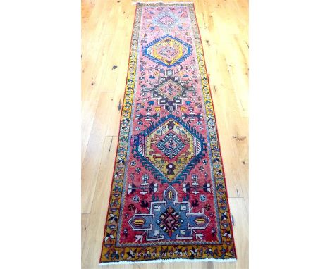 A Caucasian runner, with several medallions on a light red field, surrounded by one yellow frieze border, 310 x 85cm.