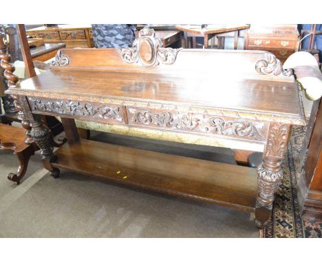 A Victorian gothic carved oak side or serving table with pediment to the back, carved freeze with floral and green man masks,