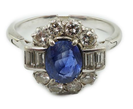 An Art Deco style platinum?, sapphire and diamond cluster ring, set with oval cut sapphire and bordered by baguette and round