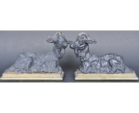 A pair of vintage 20th century ebonised black spelter ornaments portraying two reclining rams raised on a stepped brass bases