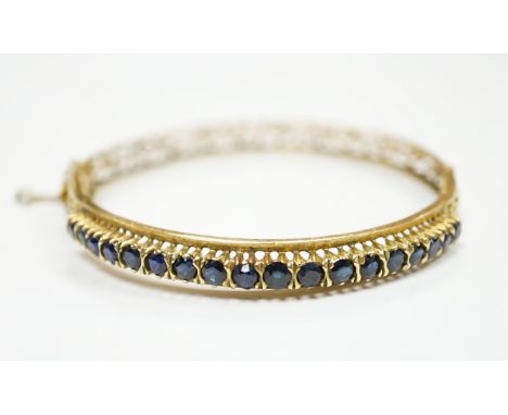 A pierced yellow metal and eighteen stone sapphire set hinged bangle, interior diameter 58mm, gross weight 14.1 grams.