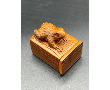 Japanese hand carved box wood netsuke sculpture of a frog sat upon a box. Fitted with black bead eyes and signed by the artis